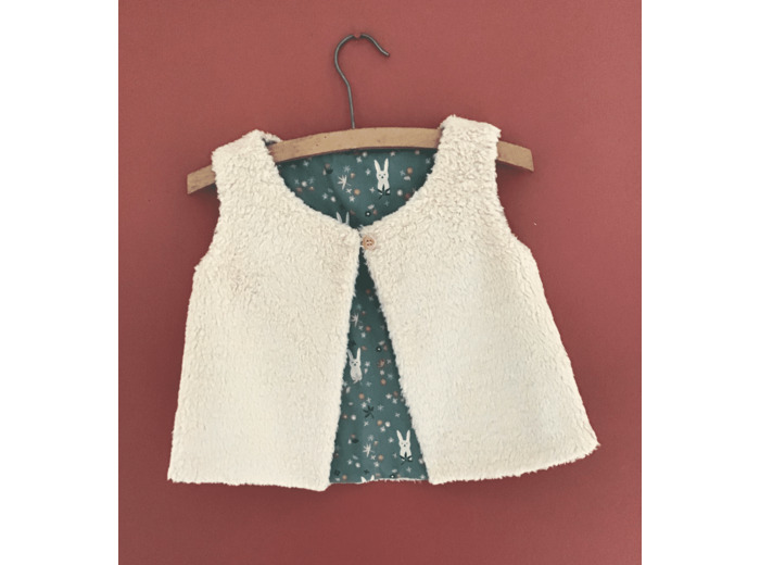 Gilet berger réversible en fausse fourrure beige et tissu coton petits lapins écrus sur fond vert .